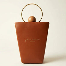Load image into Gallery viewer, A structured brown leather handbag with a gold-tone circular metal handle and a small wooden sphere accent, featuring the brand name 'Jean Paul Gaultier' printed in gold on the front, set against a plain off-white background.
