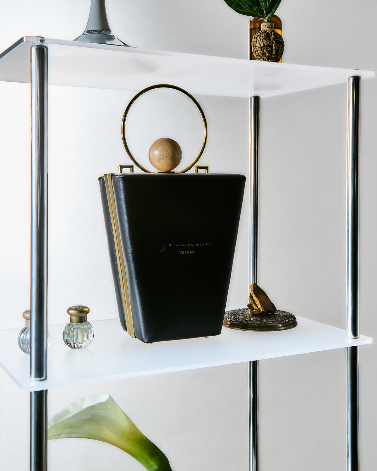 White shelf with decorative items including a black handbag, black book and a gold ring holder.